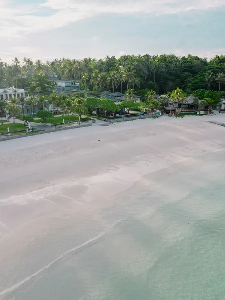 A wide stretch of resort beach with buildings set back among the trees