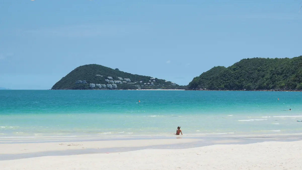 A calm beach curving toward a green headland under an open sky