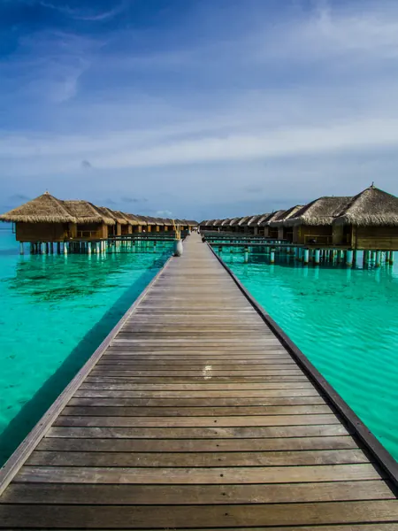 A timber jetty running out over clear water toward stilted huts