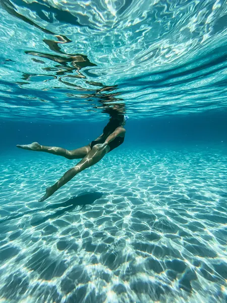 A swimmer gliding through clear shallow water over pale sand
