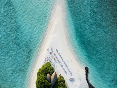 Parasols and small boats gathered along a bright sandbar from above