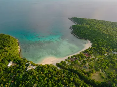 A green headland curving around a shallow turquoise cove from above