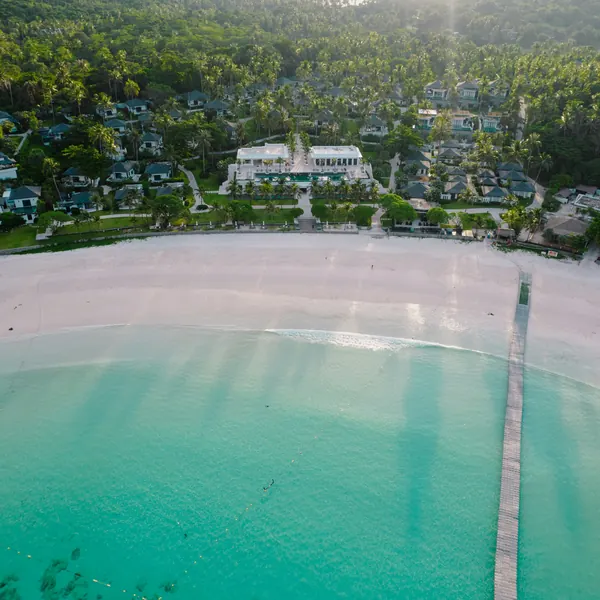 Aerial view of a long white beach with a jetty reaching into turquoise water
