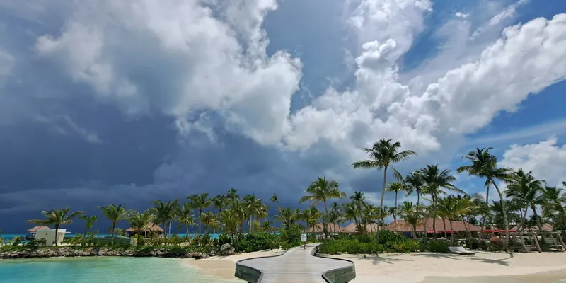 A jetty leading toward a small island under towering afternoon clouds