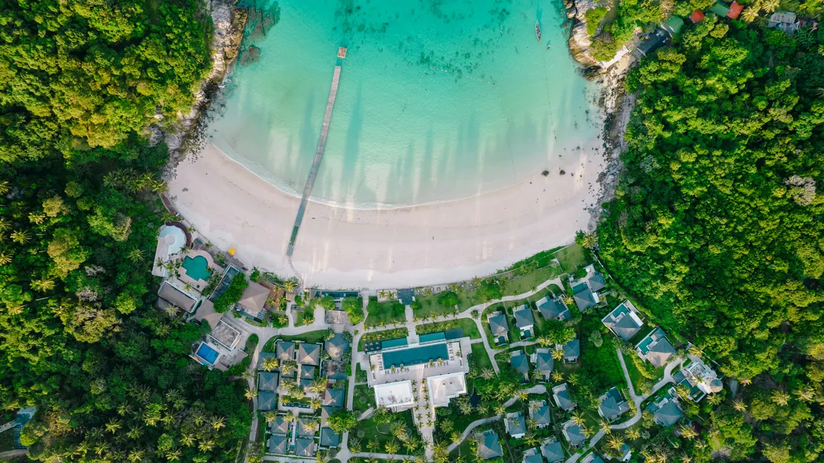 Aerial view of a turquoise cove ringed by palms and low resort cottages