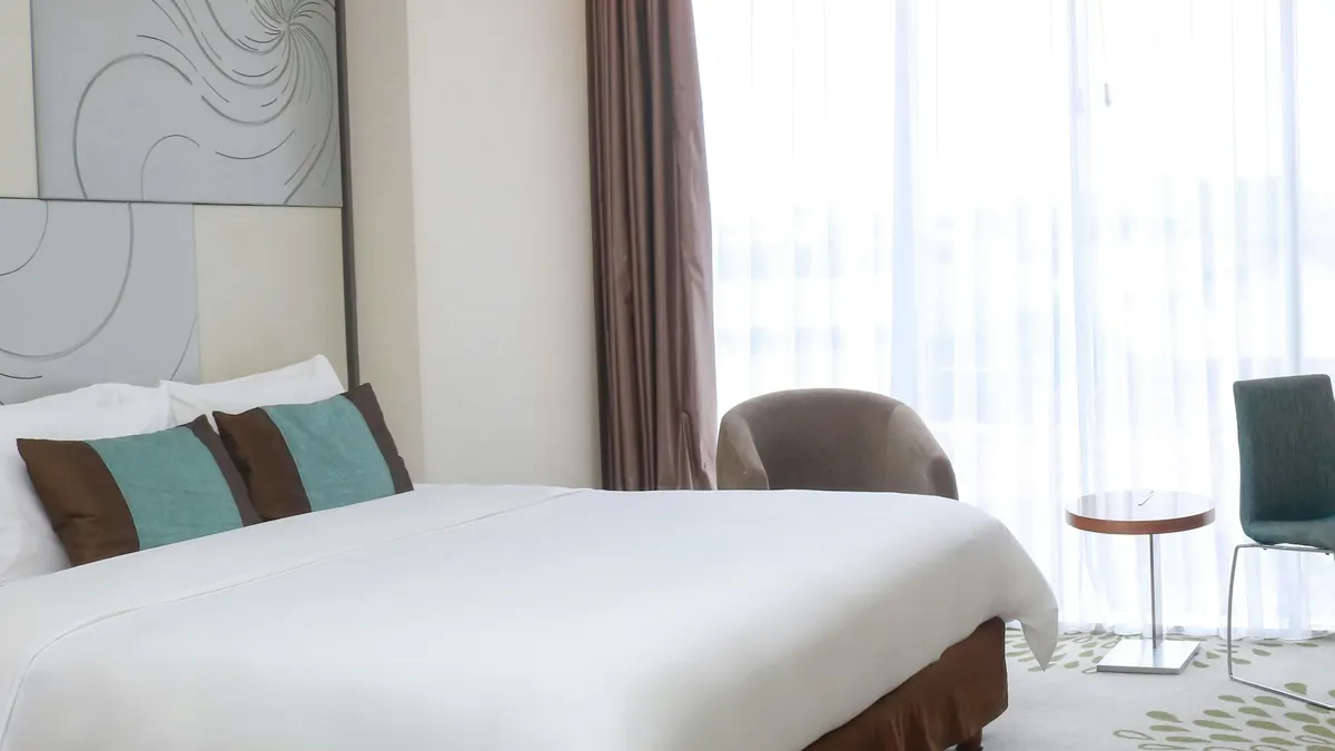 The Lagoon Room: a bed with white linen beside tall curtains opening onto a balcony