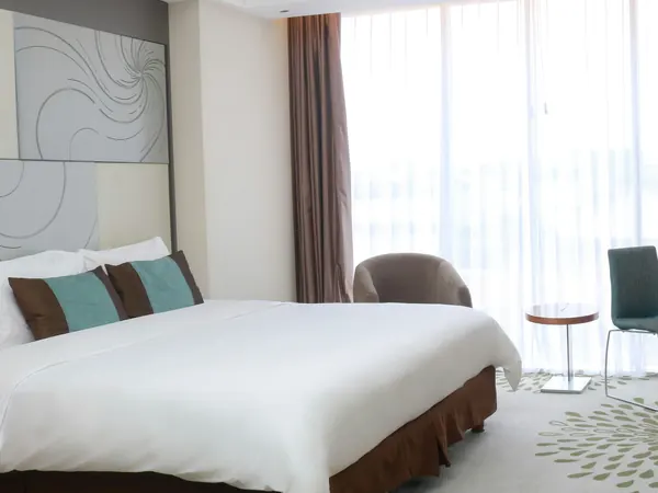 A bed with white linen beside tall curtains opening onto a balcony